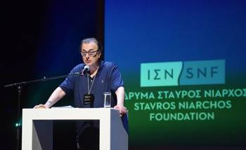 A man speaks on the podium while the logo of the Stavros Niarchos Foundation is projected behind him